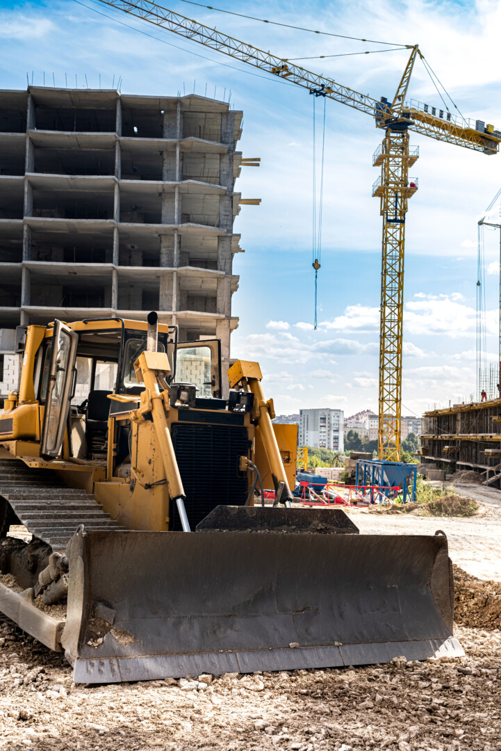 a beautiful new grader stands near a new building crane under construction