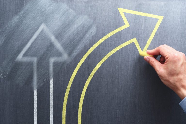 Changing business management concept. Businessman erasing white arrow and drawing yellow arrow on chalkboard. Changing business management concept. Businessman erasing white arrow and drawing yellow arrow on chalkboard.