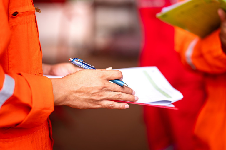Action of a safety office is writing on checklist paper during c